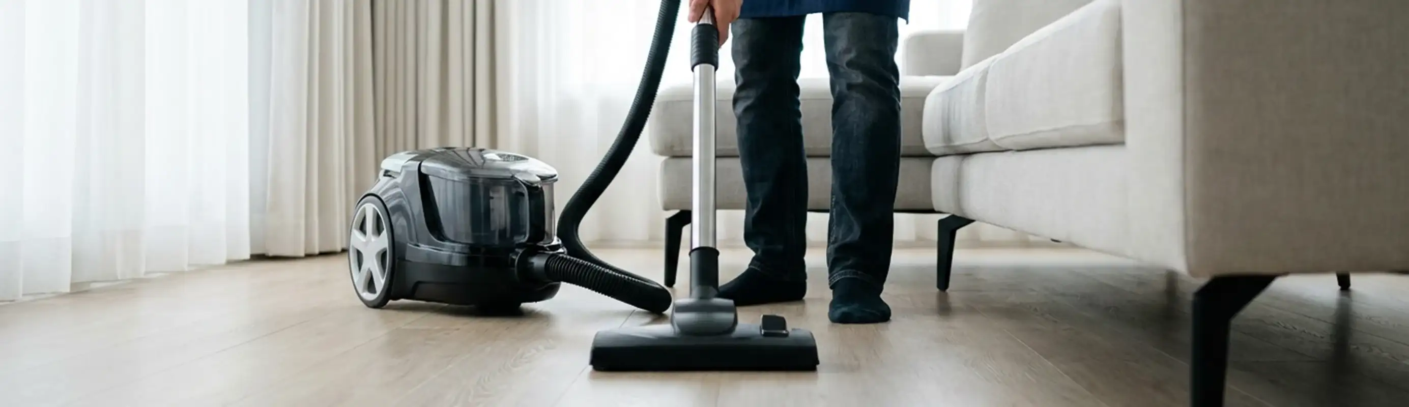 Professional house cleaner vacuuming a living room floor with a canister vacuum cleaner, Tulsa, OK.
