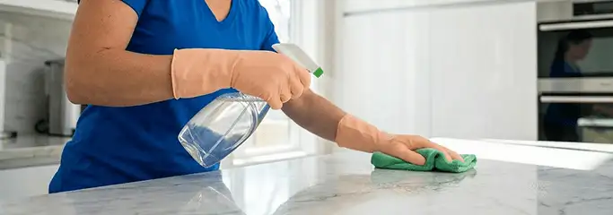 Maid service worker spraying and wiping a kitchen countertop with a microfiber cloth for sanitizing, Tulsa, OK.
