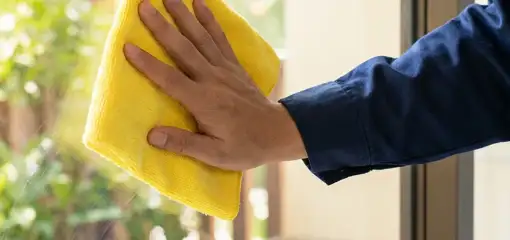House cleaner wiping a glass window with a yellow microfiber cloth for streak-free cleaning, Tulsa, OK.